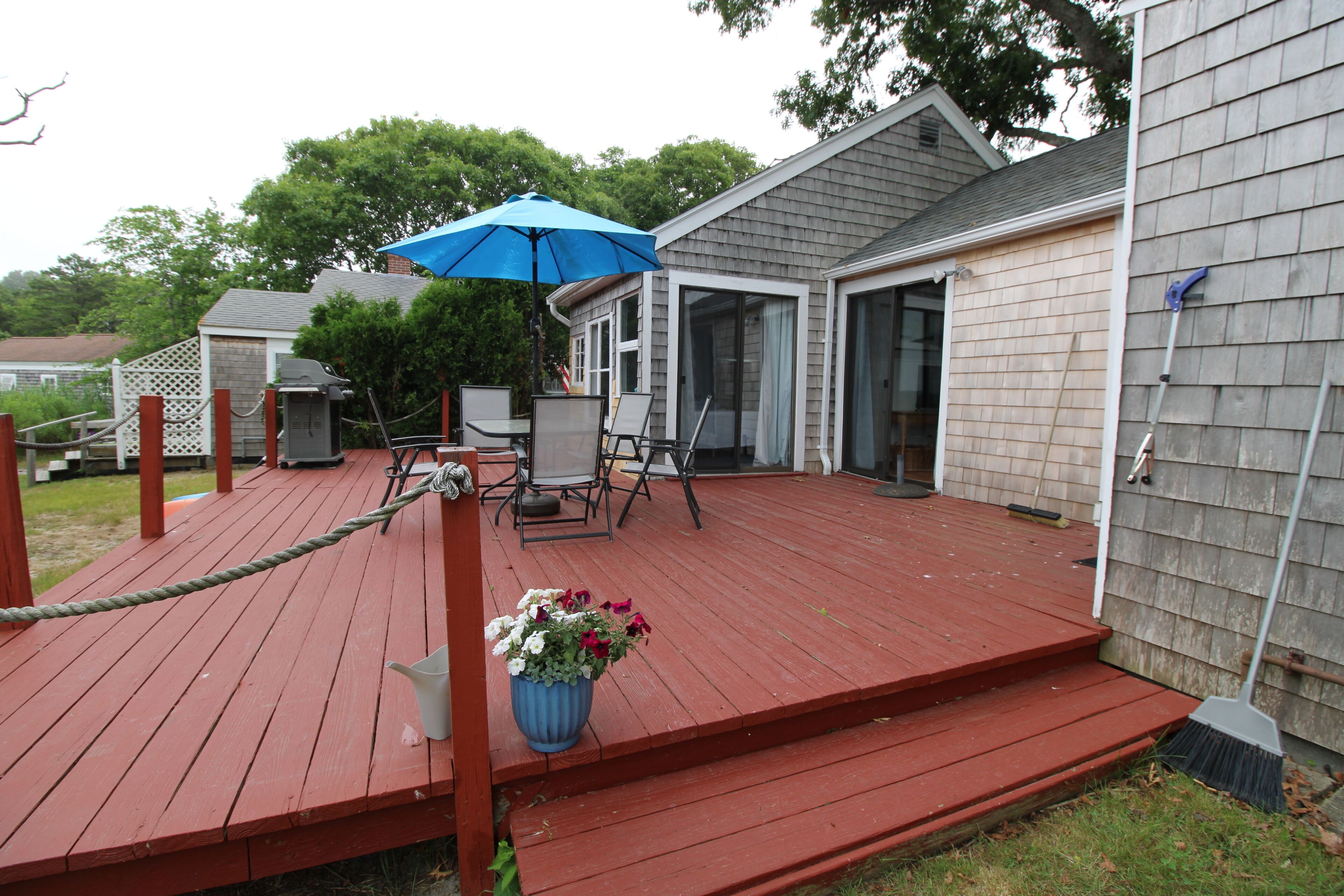 Una terraza de madera con mobiliario exterior, un paraguas azul y una planta en maceta.