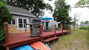 Une terrasse en bois avec des kayaks, une pagaie et un barbecue.