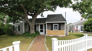 Une maison de plain-pied avec un chemin de briques menant à la porte d’entrée, entourée d’une clôture blanche en bois.