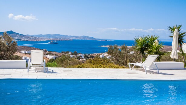 A poolside area with two white lounge chairs and a view of the sea and distant mountains. - Ocean View house with swimming pool ISLA summer homes (Paros)