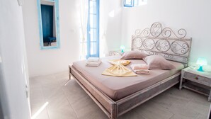 A neatly made bed with pillows and a folded towel, a bedside table with a lamp, and a mirror on the wall. - Ocean View house with swimming pool ISLA summer homes (Paros)