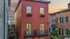 A red brick building with multiple windows, a balcony with plants, and a small garden area. - Private Heated Pool | 5*Clean | Flex Cancelation (Savannah)