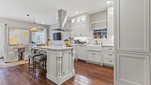 A modern kitchen with white cabinetry, a central island, and a dining area with a chandelier. - Private Heated Pool | 5*Clean | Flex Cancelation (Savannah)