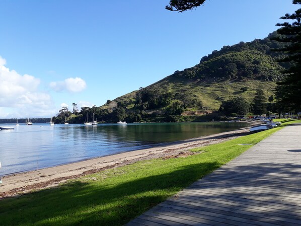 A wooden boardwalk along a lake with boats and a hilly backdrop.