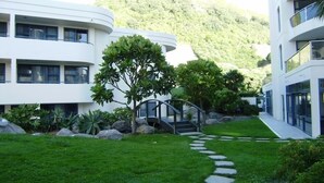 A modern building with a curved facade, a stone pathway, and a small bridge leading to a building entrance.