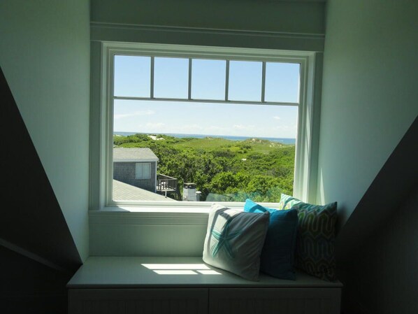 A room with a window seat overlooking a green landscape.