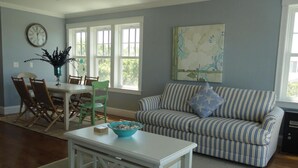 Un salon avec un canapé à rayures, une table à manger, des chaises, une horloge et un tableau accroché au mur.