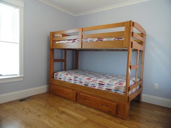 Un lit superposé avec un lit inférieur et un tiroir de rangement, placé contre un mur bleu clair, avec une fenêtre sur la gauche.