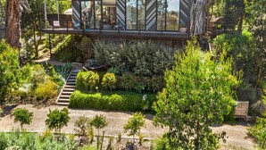 A modern house with a glass balcony, surrounded by lush greenery and a stone pathway. - Tucker House (Wye River)