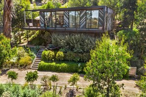 Ein modernes Haus mit einem Glasbalkon, umgeben von üppigem Grün und einem Kiesweg.