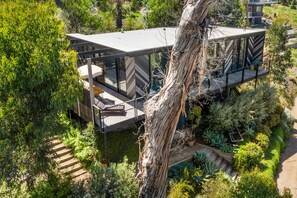 Ein modernes Haus mit mehrstöckigem Design, umgeben von üppigem Grün und einem Baumstamm.
