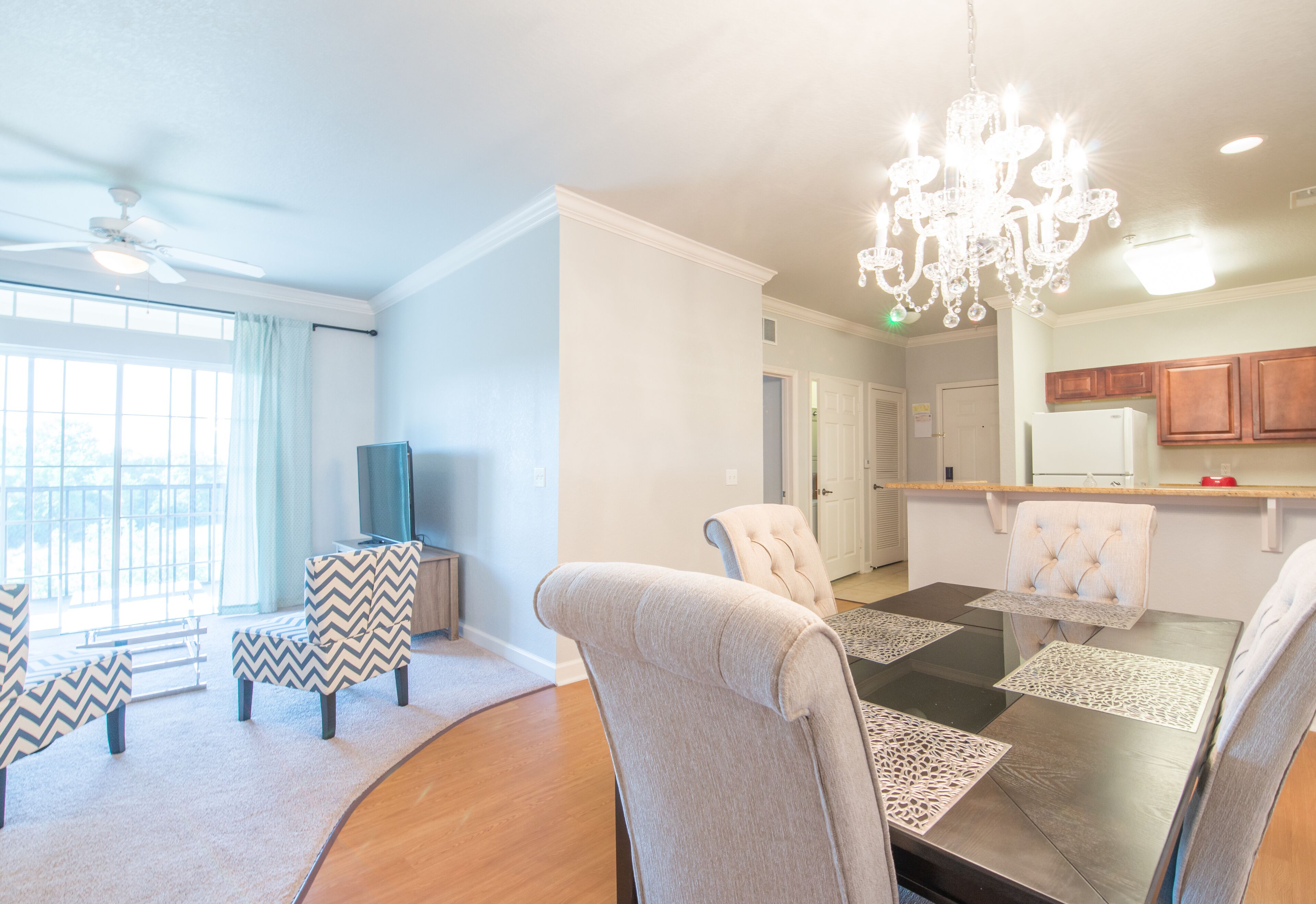 Een moderne woonkamer met een eethoek, een kroonluchter en een keuken op de achtergrond.