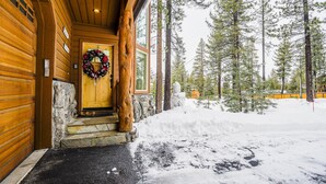 Entrada a una cabaña de madera con un adorno de guirnalda, escalones de piedra y un camino de entrada cubierto de nieve.