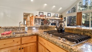 Una cocina moderna con encimeras de granito, estufa a gas, armarios de madera y chimenea de piedra.