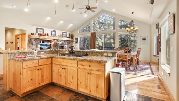Una cocina amplia con armarios de madera, encimeras de granito y una isla grande. Varias ventanas ofrecen luz natural y vistas al exterior.
