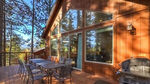 Una terraza de madera con una mesa, sillas, ventanas amplias y una parrilla.