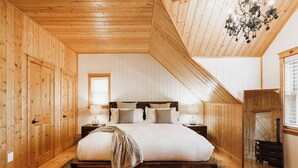 Ein Schlafzimmer mit Holzvertäfelung, einem großen Bett, zwei Nachttischen, einer Chandelier und einem Kleiderschrank.