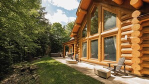 Eine Blockhütte mit großen Fenstern, einer Terrasse mit Gartenmöbeln und einem gepflegten Rasen.