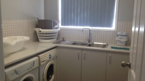 Een compacte keuken met een wasmachine, een spoelbak en een raam met zonwering.