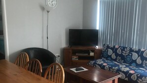 Een woonkamer met een houten eettafel, stoelen, een bank, een televisie en een klok aan de muur.