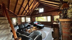 A log cabin interior with a wooden ceiling, a fireplace, a leather sofa set, and a dining table. - Creekside Cabin near falls, casino, golf, & more! (East Stroudsburg)