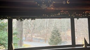 A cozy cabin interior with a large window, a leather sofa, and a wooden table. - Creekside Cabin near falls, casino, golf, & more! (East Stroudsburg)