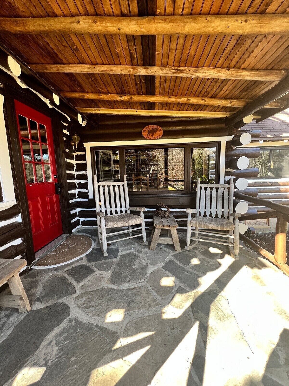 A log cabin with a red door, stone flooring, and wooden benches.