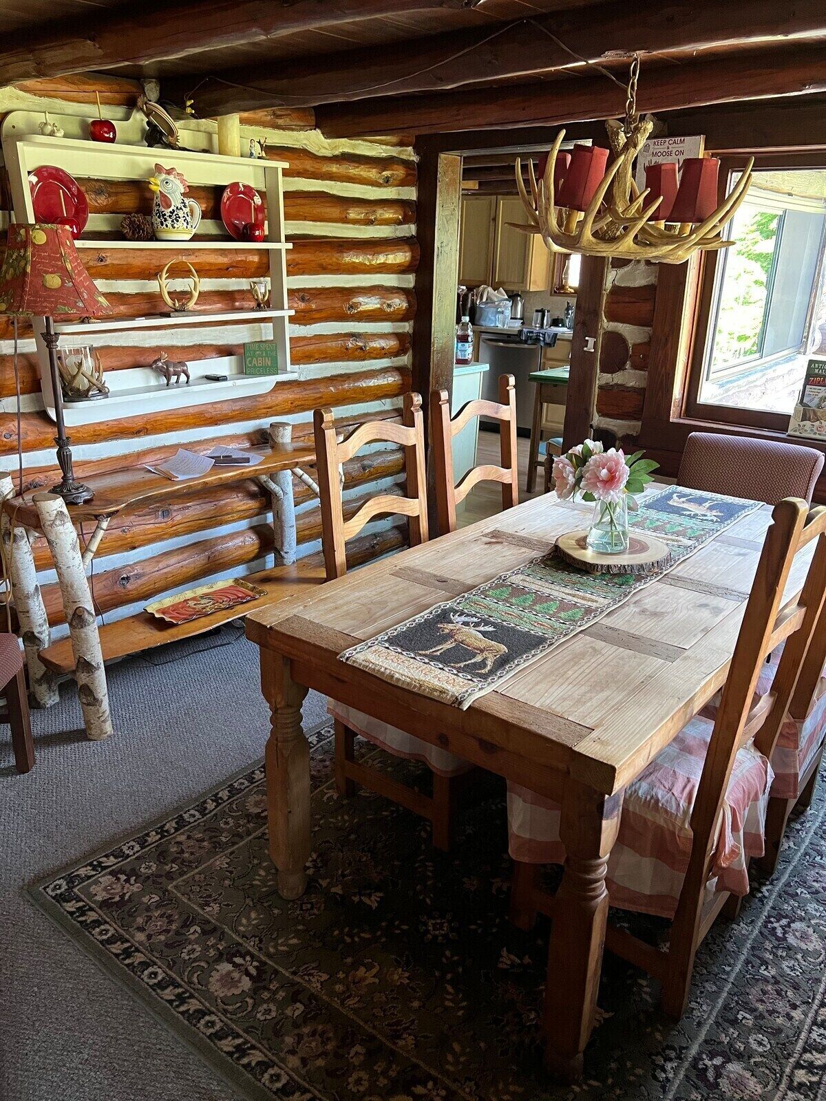 Ein rustikales Cabin-Interieur mit einem Holztisch, Stühlen, einer Chandelieber und einer Wand aus Baumstämmen.