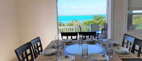 Mesa de comedor para cuatro personas, con platos, vasos y cubiertos, con vistas a un paisaje marino.