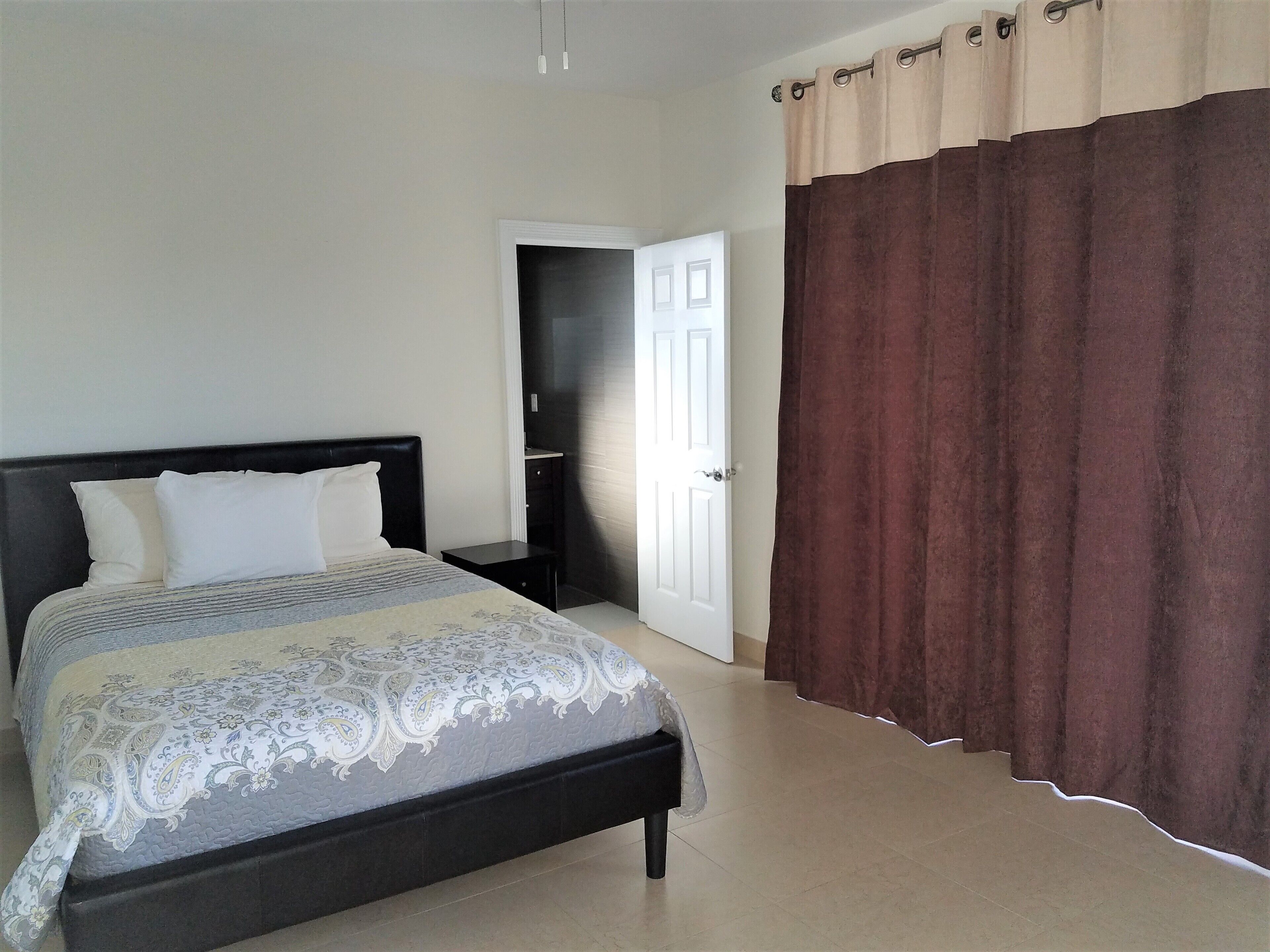A bedroom with a bed, a nightstand, a door, and a curtain.