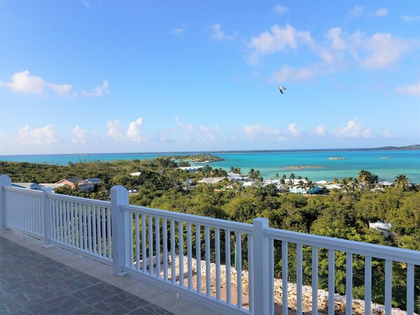 A coastal view with a white balcony railing, a clear sky, and a turquoise sea.