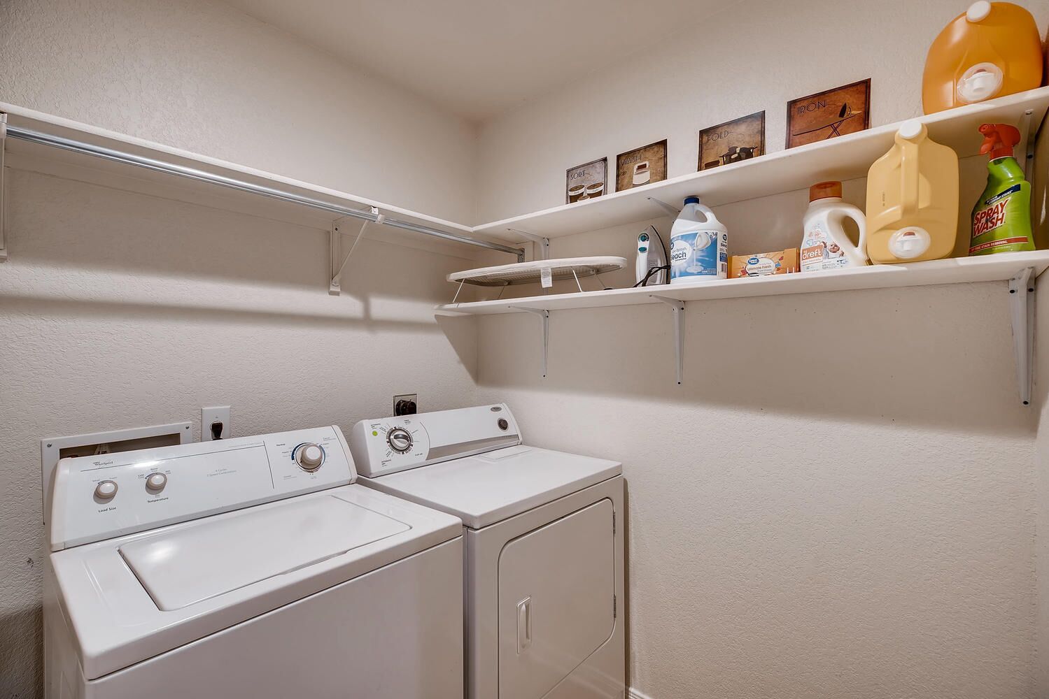 A laundry area with two washing machines and shelves above containing cleaning supplies.