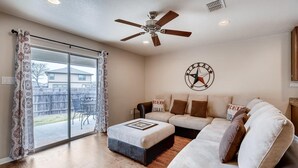 Una sala de estar con un sofá modular, un ventilador de techo y un ventanal con cortinas estampadas.