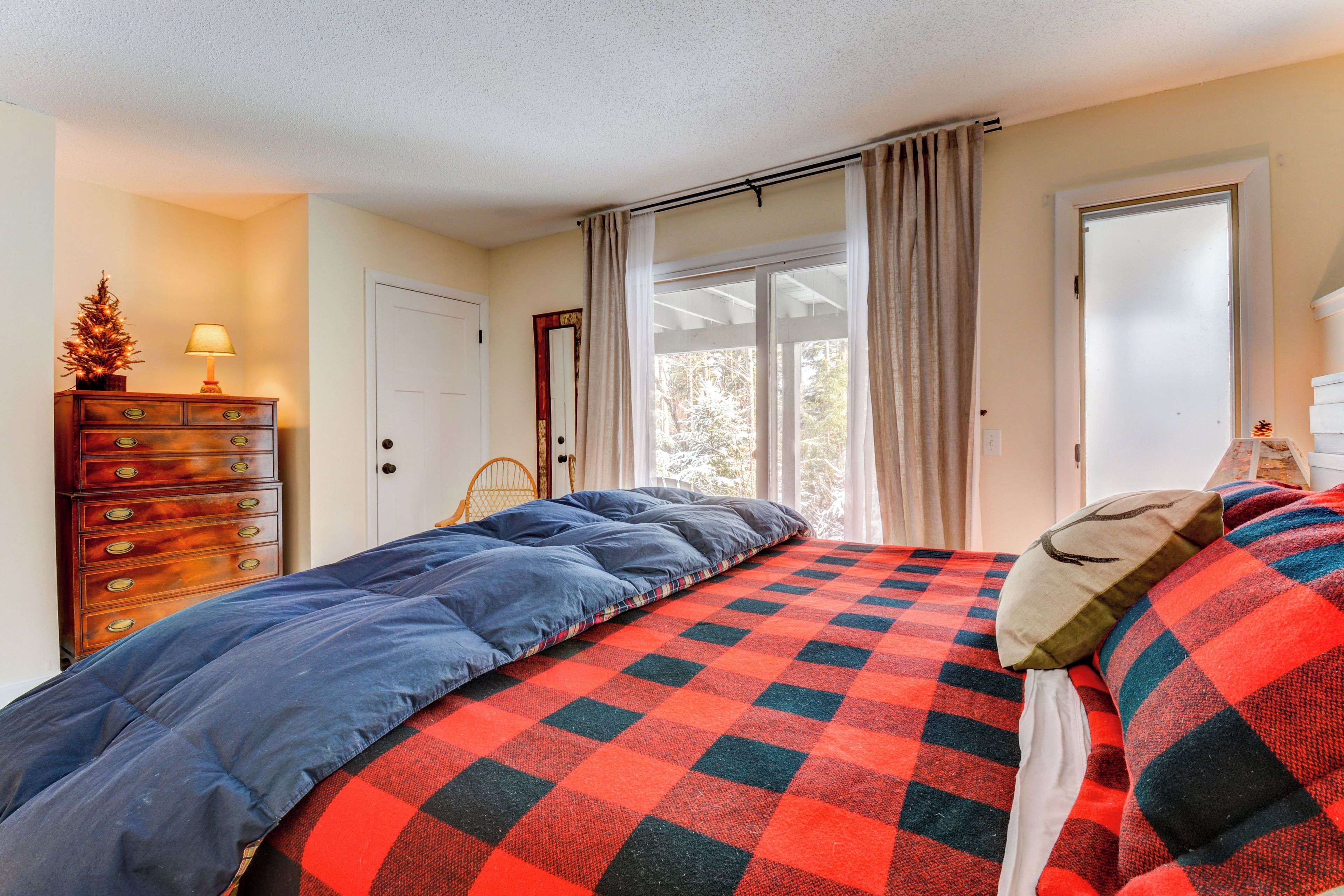 Um quarto com uma cama, cômoda, janela com cortinas e porta.