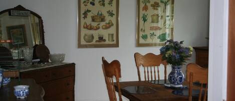 A dining room with a wooden table, chairs, a vase with flowers, and two framed botanical prints on the wall.