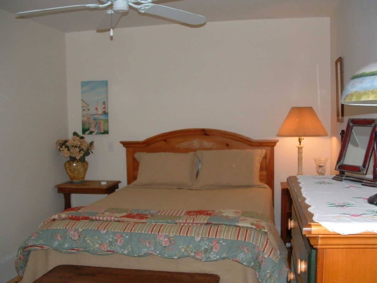 Ein Schlafzimmer mit Bett, Nachttisch, Lampe, Blumenvase und einem Bild an der Wand.