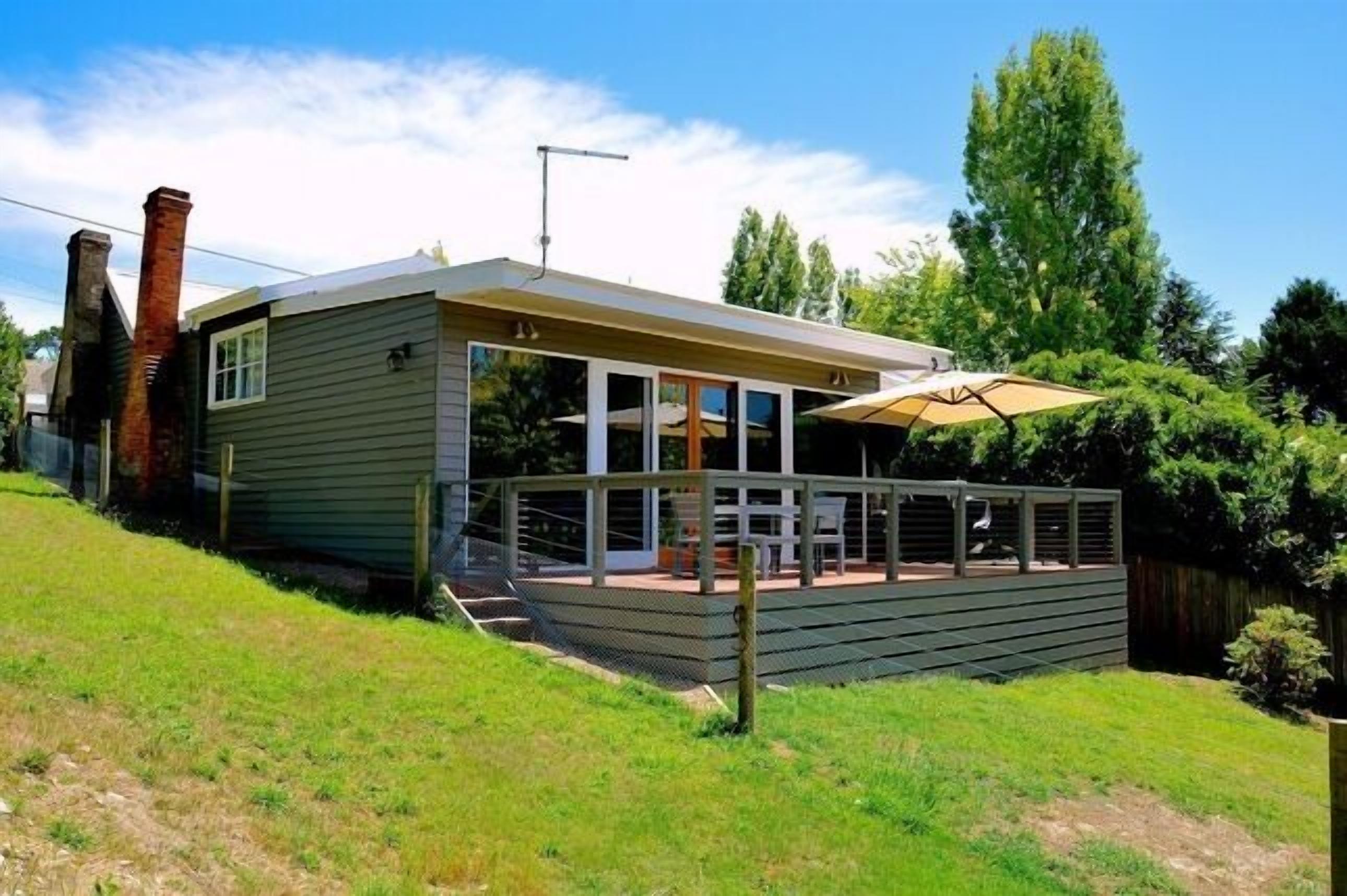 A modern house with a deck, a chimney, and a large window overlooking a grassy yard.