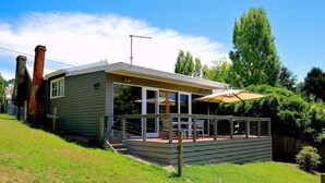 A modern house with a deck, a chimney, and a large window overlooking a grassy yard. - Waterside Cottage - Perfect Lakeside Location (Daylesford)