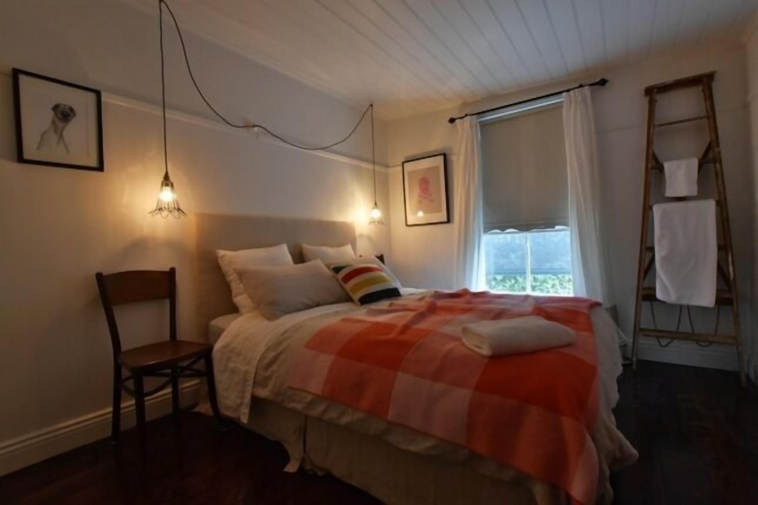 A bedroom with a bed, a chair, a ladder, and a window with curtains.