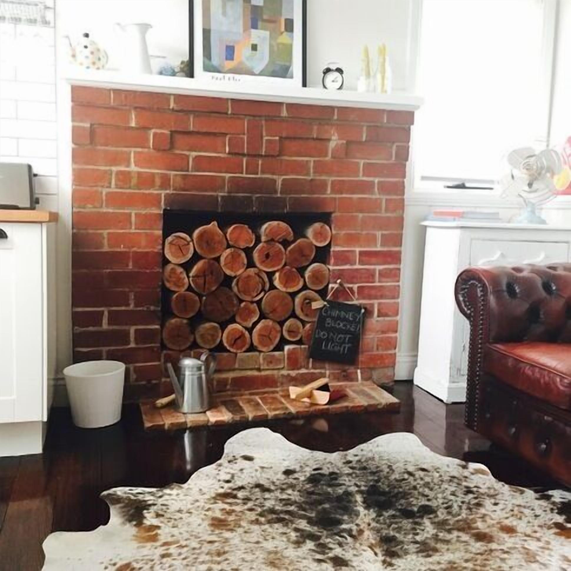 A fireplace with stacked logs, a sign advising against lighting it, and a cowhide rug on the floor.