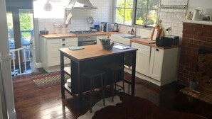 A modern kitchen with white cabinetry, a wooden island, and a brick fireplace. - Waterside Cottage - Perfect Lakeside Location (Daylesford)