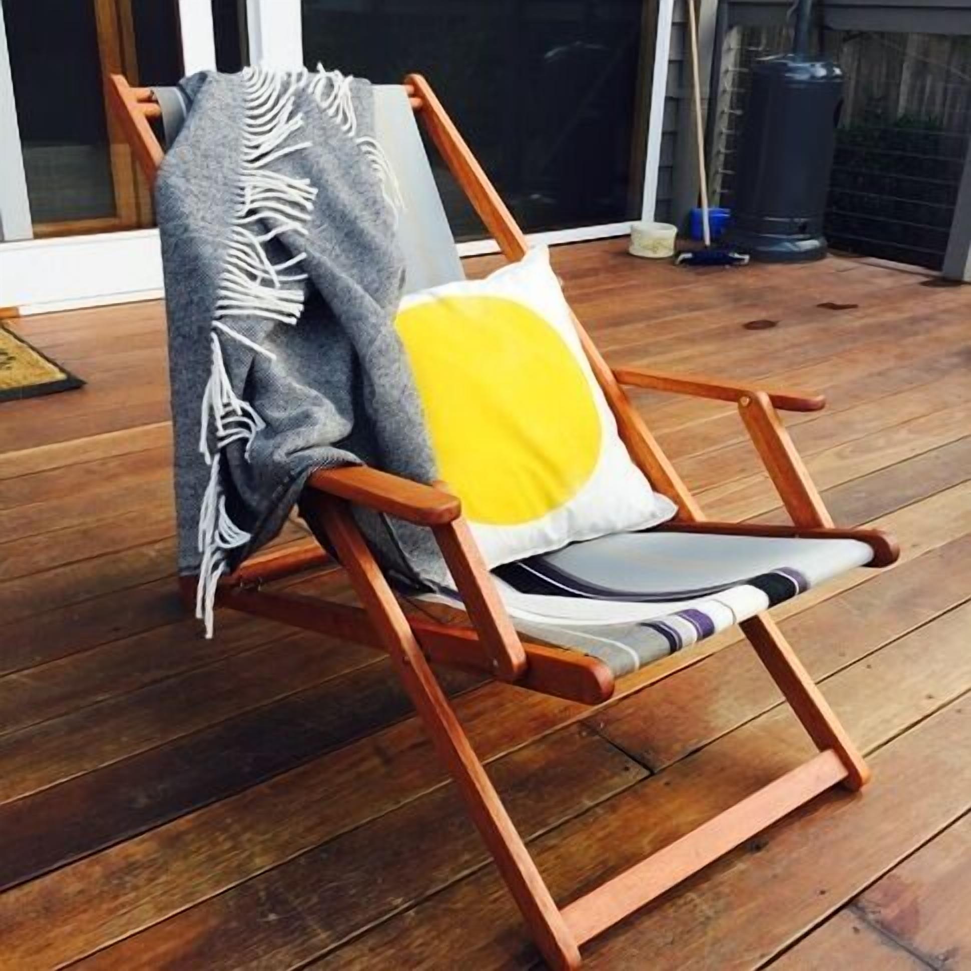 A wooden deck chair with a cushion and a throw blanket.
