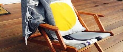 A wooden deck chair with a cushion and a throw blanket.