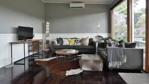 A modern living room with a grey sofa, a coffee table, and a television. - Waterside Cottage - Perfect Lakeside Location (Daylesford)