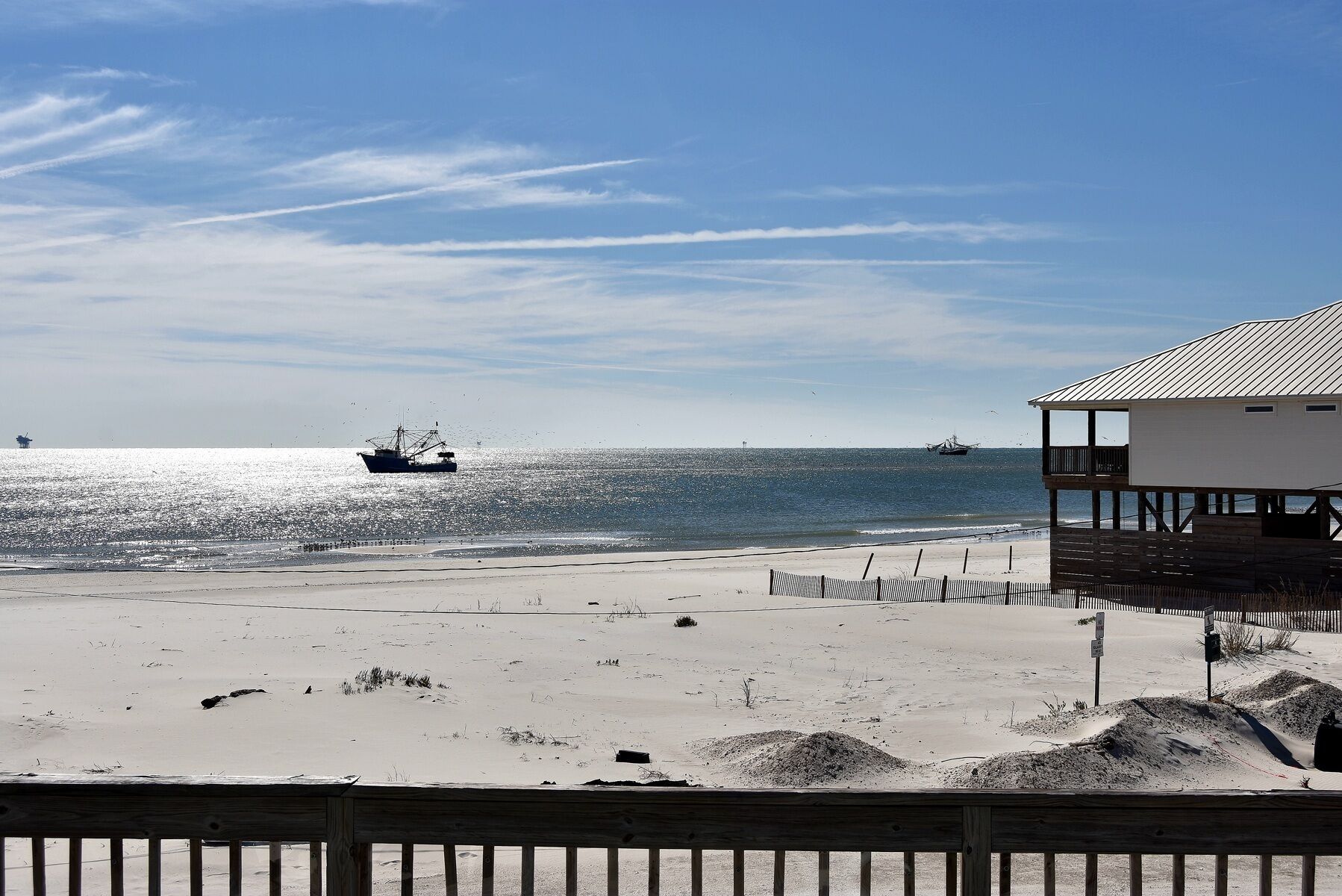A beach with a wooden fence, a building with a balcony, and two boats on the water.
