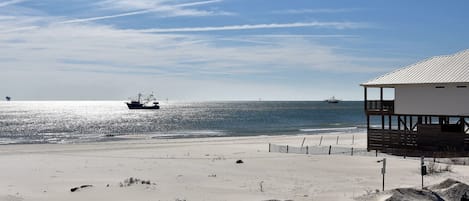 A beach with a wooden fence, a building with a balcony, and two boats on the water.