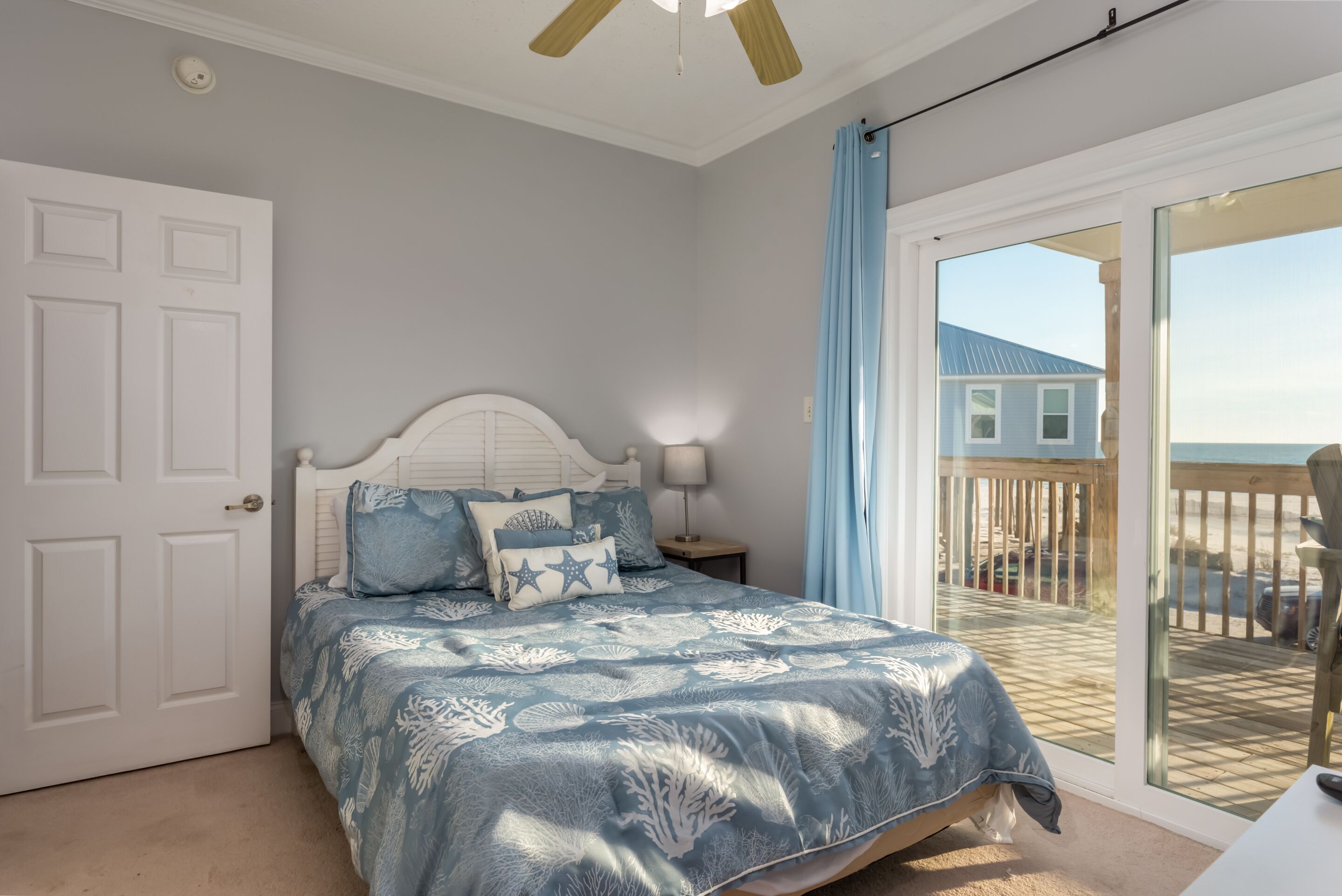 Une chambre avec un lit, une table de chevet, un ventilateur de plafond, une porte-fenêtre coulissante donnant sur un balcon et une vue sur la plage.