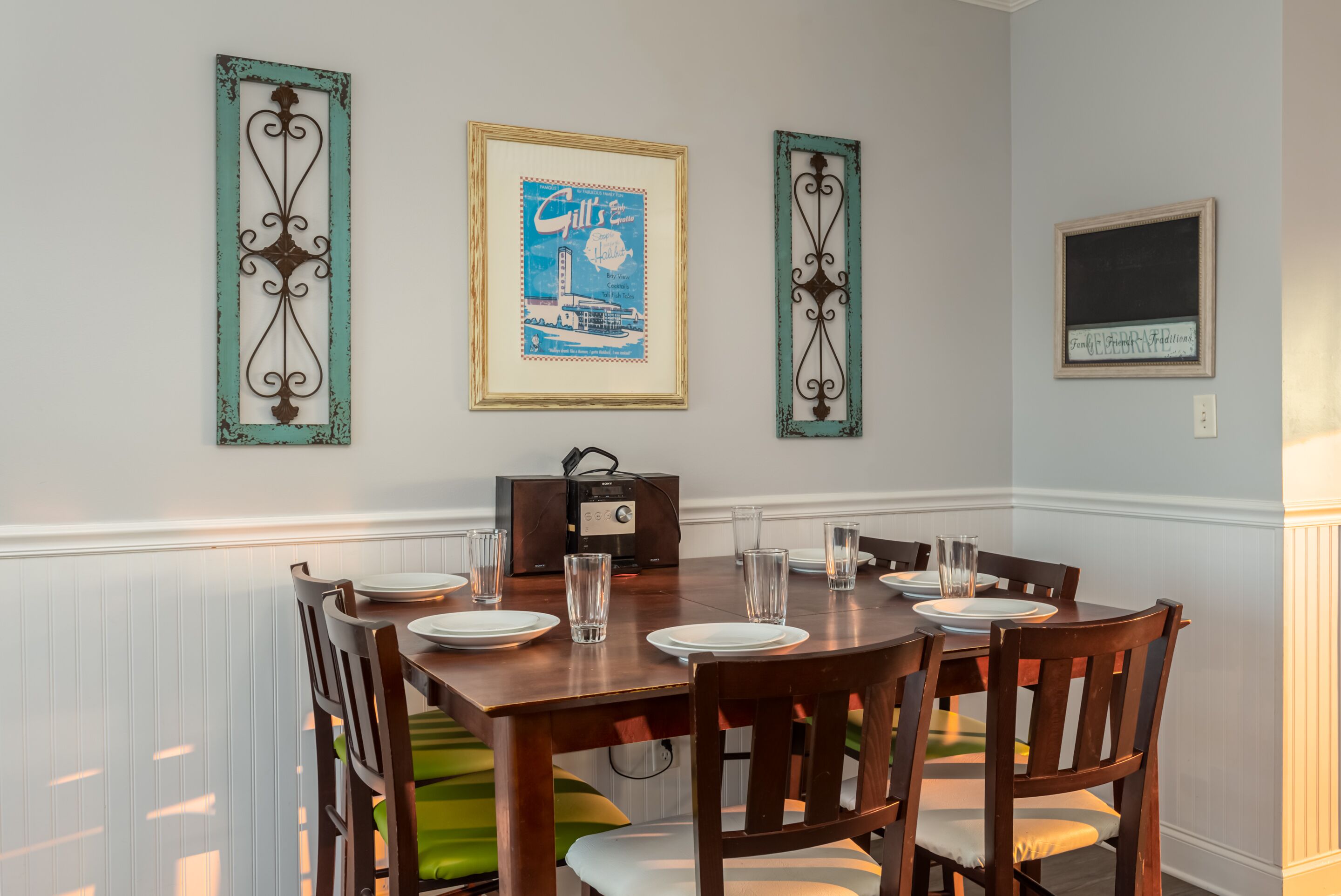 A dining area with a wooden table set for four, surrounded by chairs with green cushions.