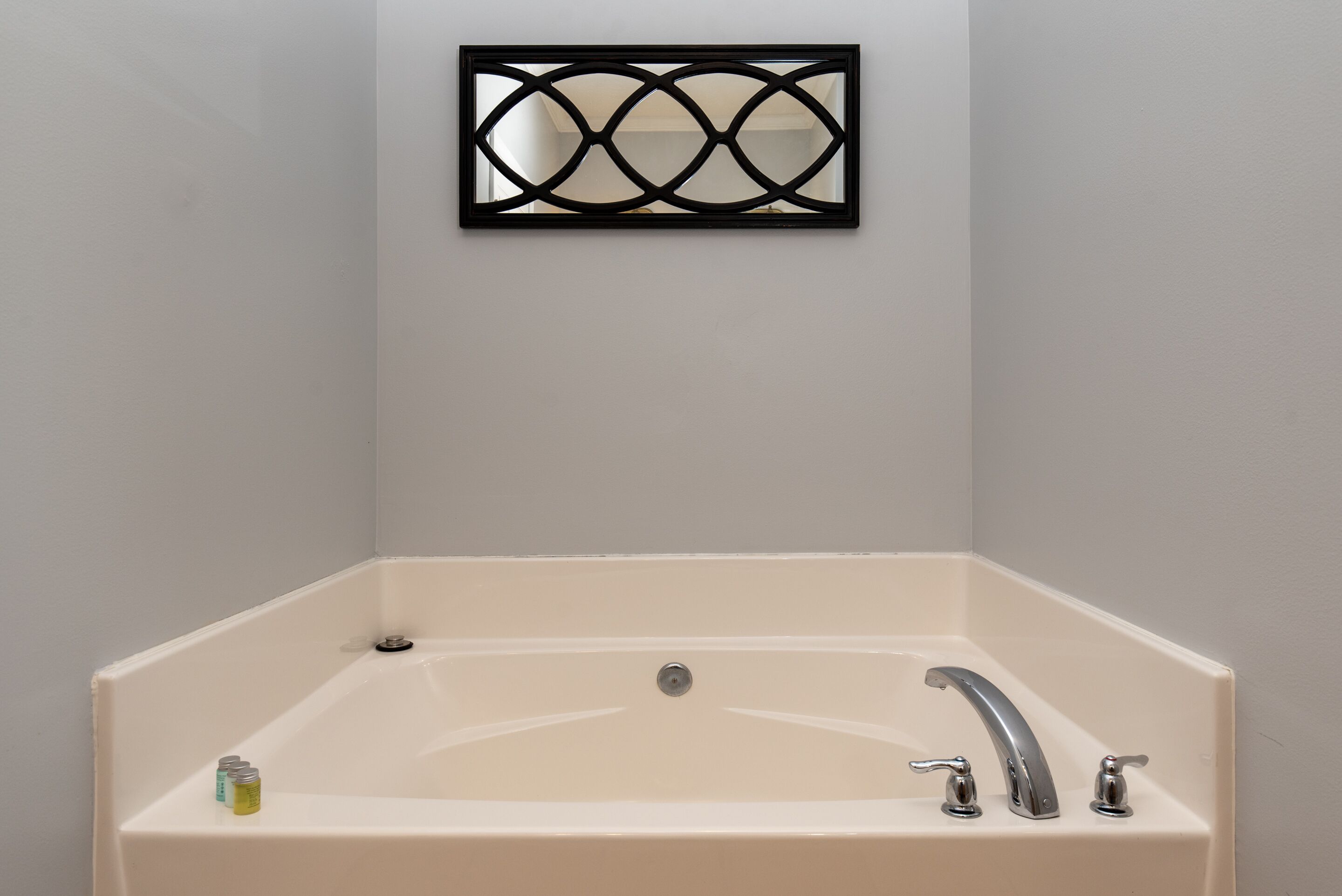 A rectangular bathtub with a single faucet and a drain, positioned against a plain wall.