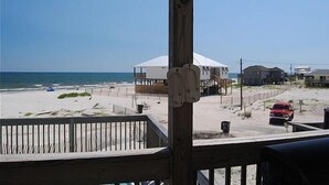 Une vue sur la plage avec une terrasse en bois, une tente blanche et une voiture rouge garée sur le sable.